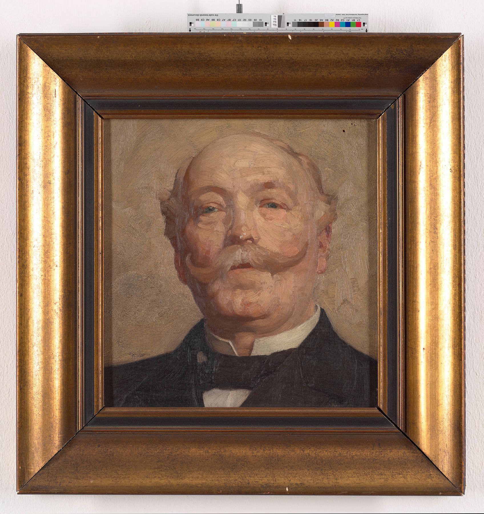 Frontales Büstenportrait eines Mannes mit Schnurrbart in einem dunklen Anzug vor hellem Hintergrund