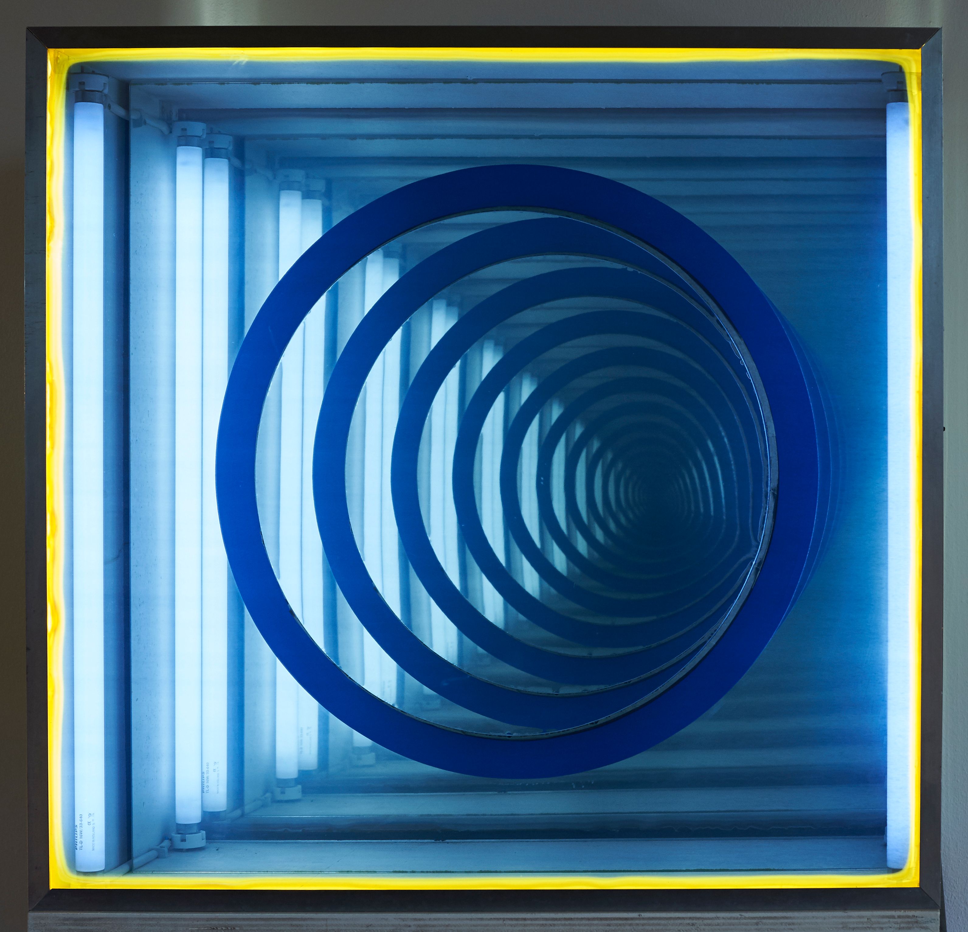 Hinter einem halbdurchlässigen, bläulichen Spiegel mit gelber Umrandung befindet sich ein blauer Ring. Der Spiegel wird in diesem Ring elektronisch in Bewegung versetzt, sodass es zu einer optischen Veränderung und Vervielfältigung der Ringe kommt.