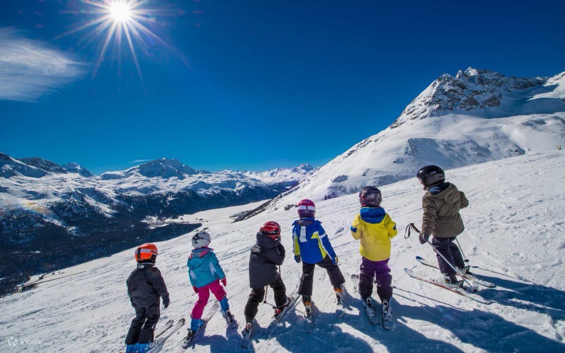 An instructor and a line of children in ski gear looking out over a snowy valley