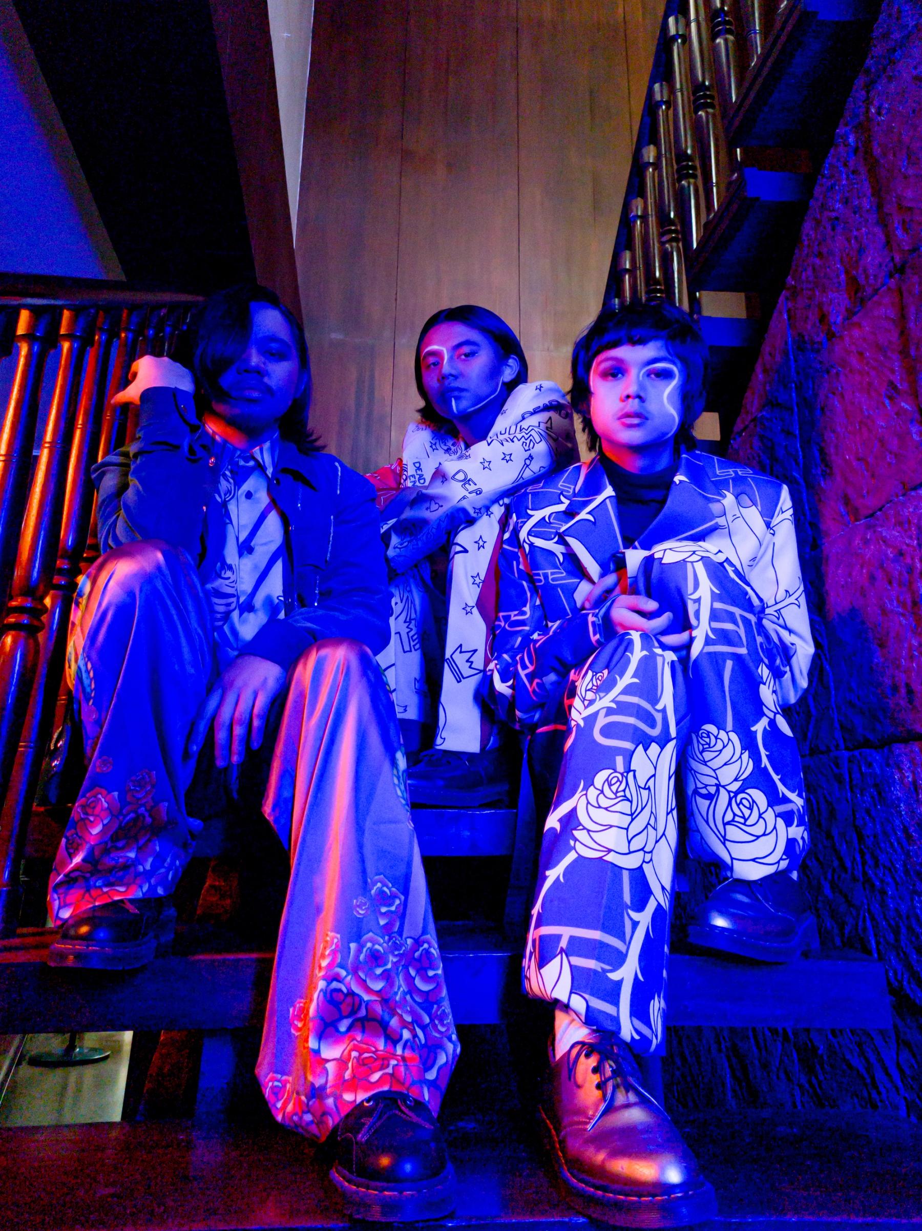 IV of spades are seated on a staircase in pink, blue, and purple lighting