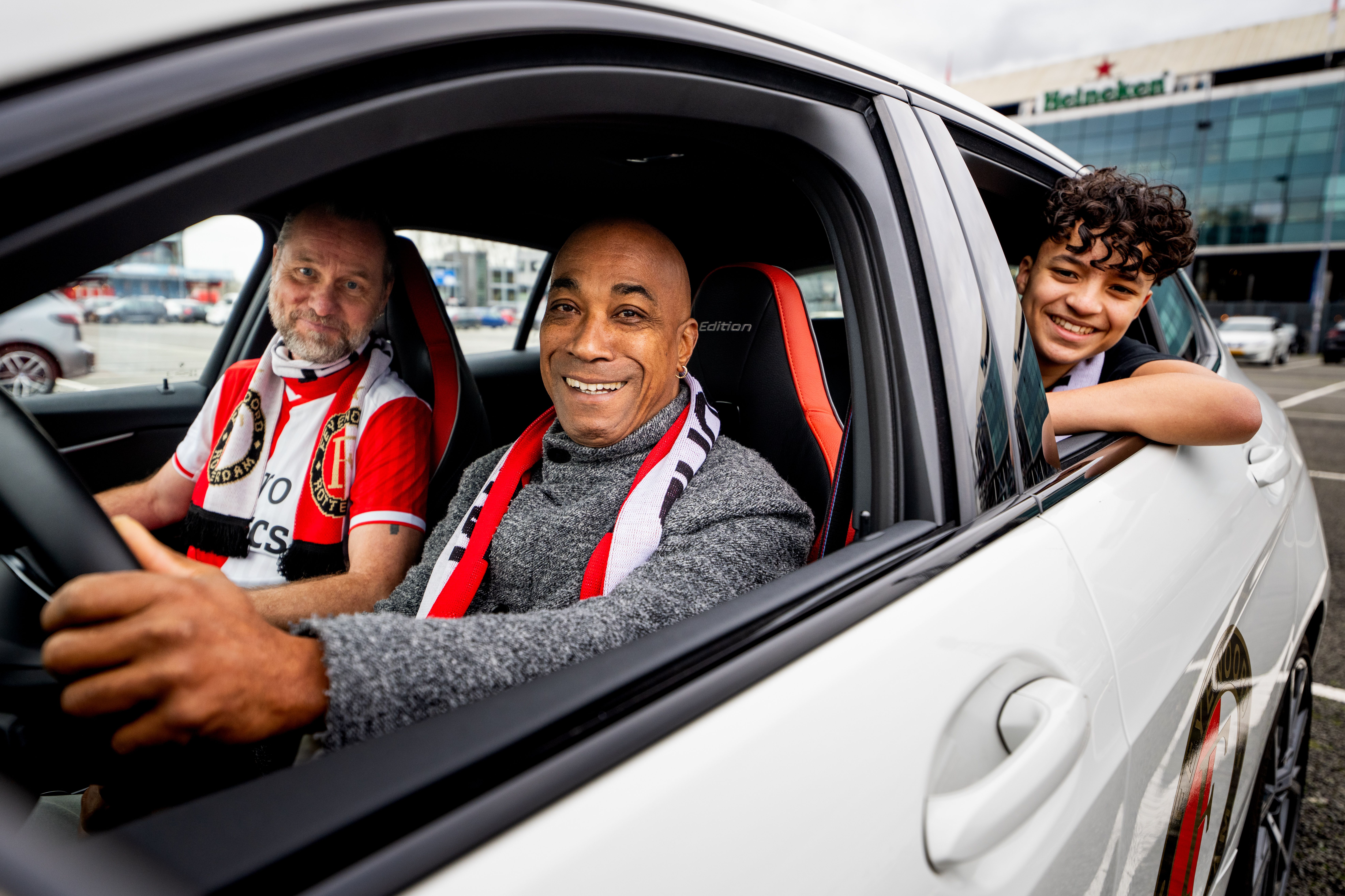 Afbeelding van drie Feyenoord-supporters in een auto voor De Kuip (Feijenoord Stadion)