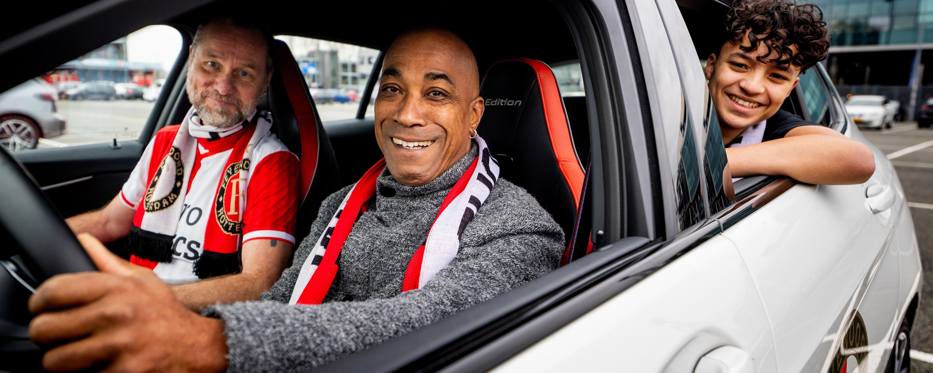 Afbeelding van drie Feyenoord-supporters in een auto voor De Kuip (Feijenoord Stadion)