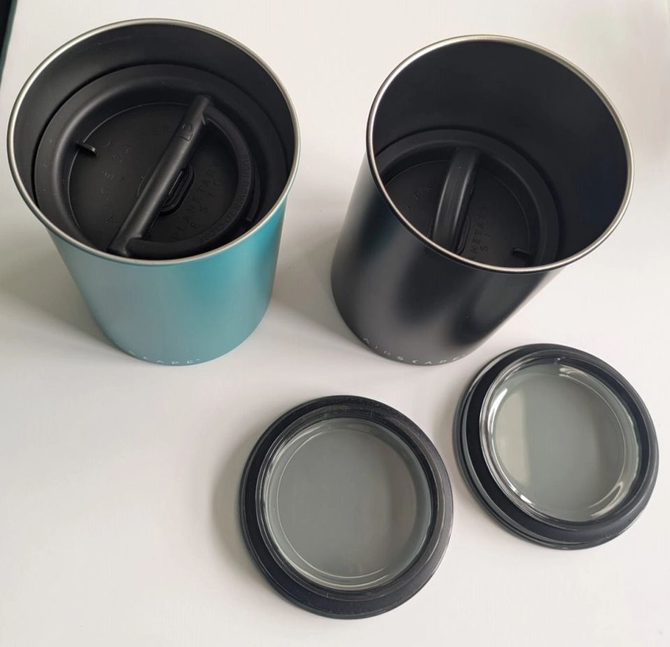 Two open Airscape coffee canisters with black inner lids at different heights and transparent outer lids in front.