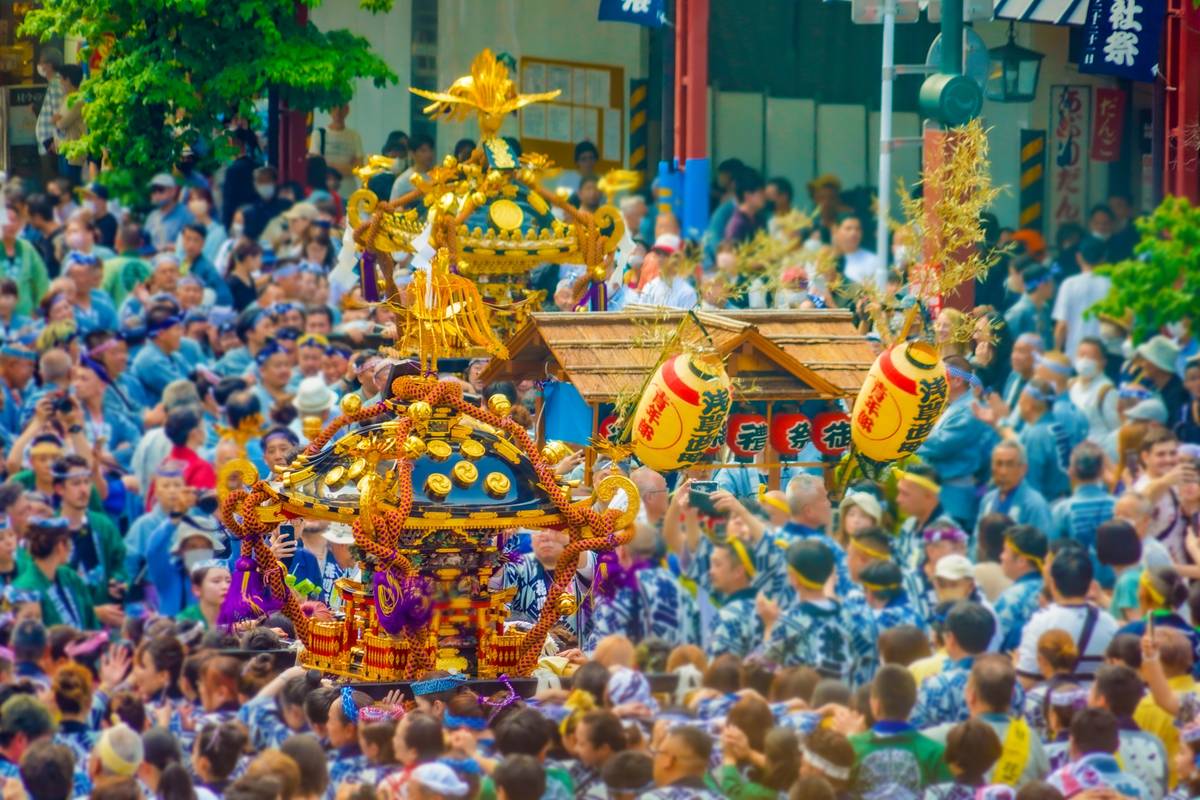 A crowded Japanese festival with people carrying ornate golden mikoshi shrines and lanterns.