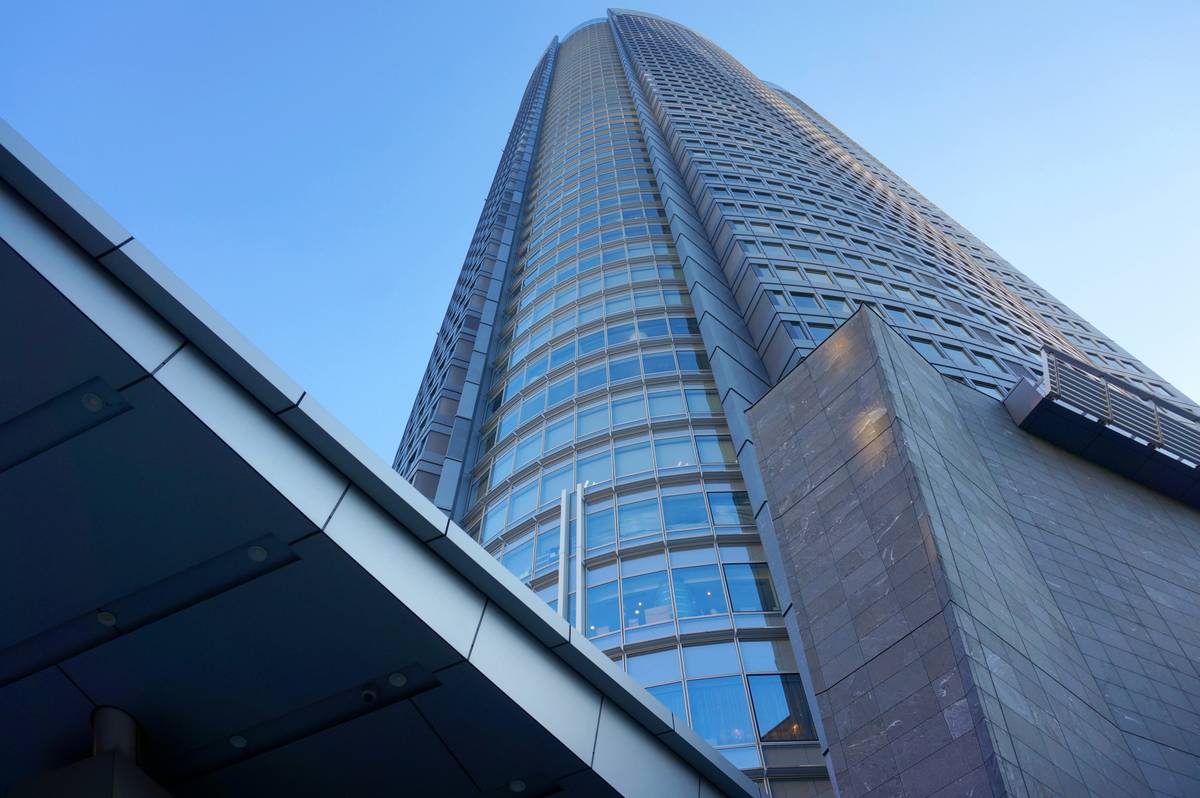 Low-angle view of a modern skyscraper with curved glass and angular stone facades against a clear blue sky.
