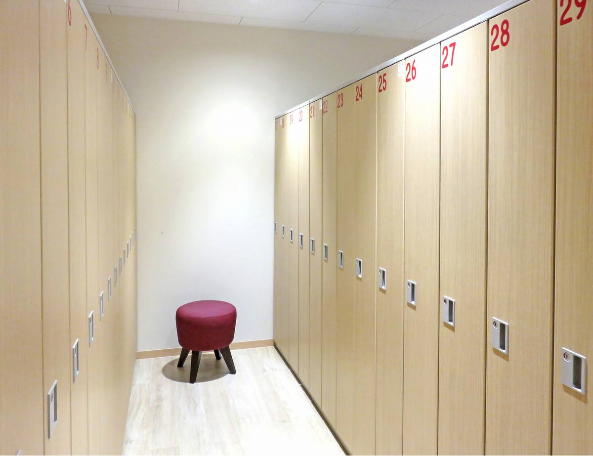 Light wood locker room with red numbered lockers and a maroon stool.