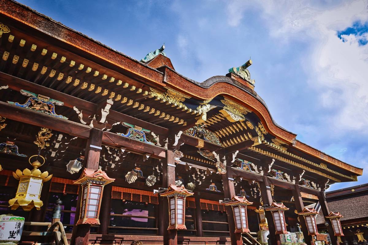 Ornate wooden Japanese temple with a curved roof and hanging lanterns under a blue sky.