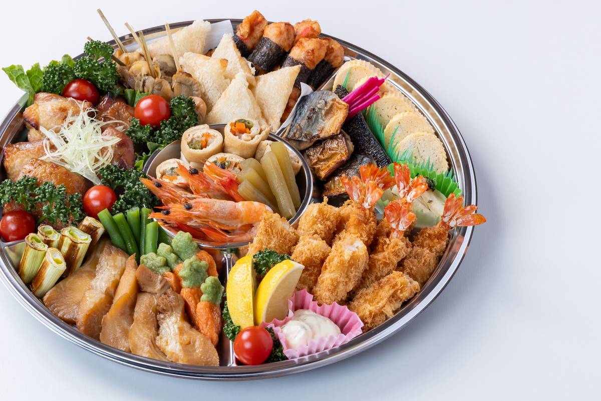 A large round silver platter showcasing a variety of colorful Japanese dishes.