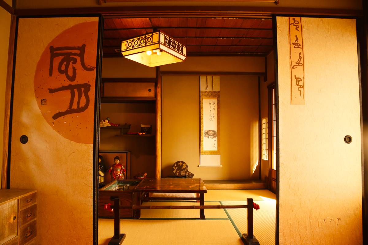 A traditional Japanese room with tatami mats, a low table, and sliding paper doors featuring calligraphy and a red circular design, lit by a lantern.