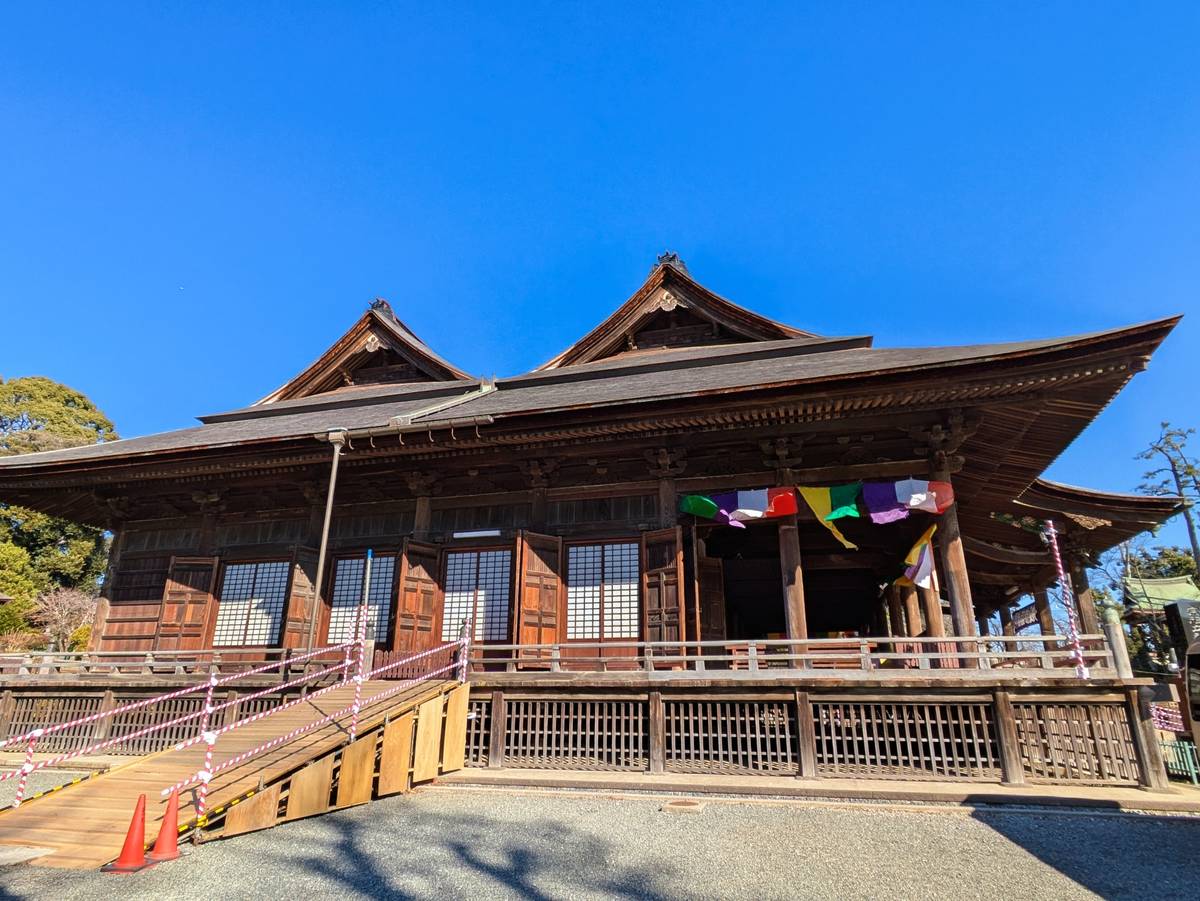 Traditional wooden Japanese temple with tiered roofs, a wooden ramp, and colorful prayer flags under a clear blue sky.