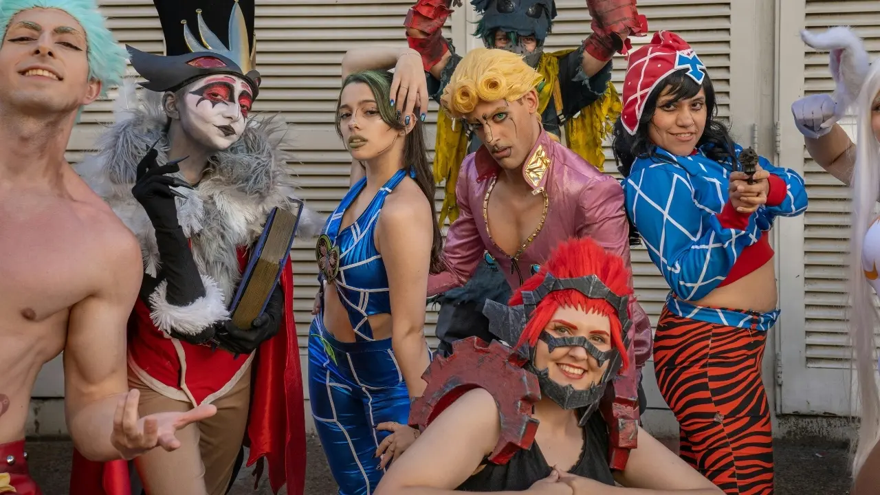 A group of cosplayers, many dressed as JoJo's Bizarre Adventure characters, smiles while posing for a photo.