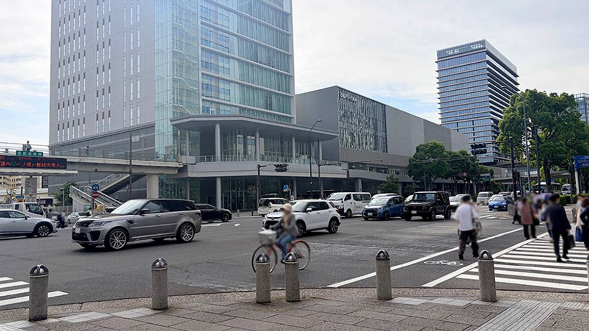 A busy urban street scene with modern high-rise buildings, cars, and pedestrians.