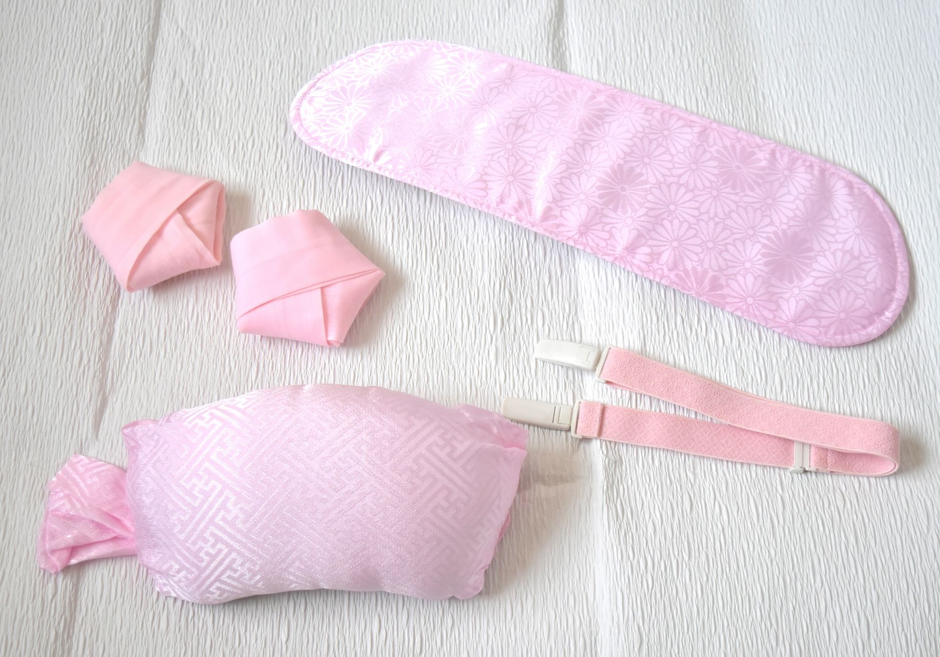 Pink fabric accessories: a long padded band with a subtle floral pattern, a rectangular pillow with a geometric pattern