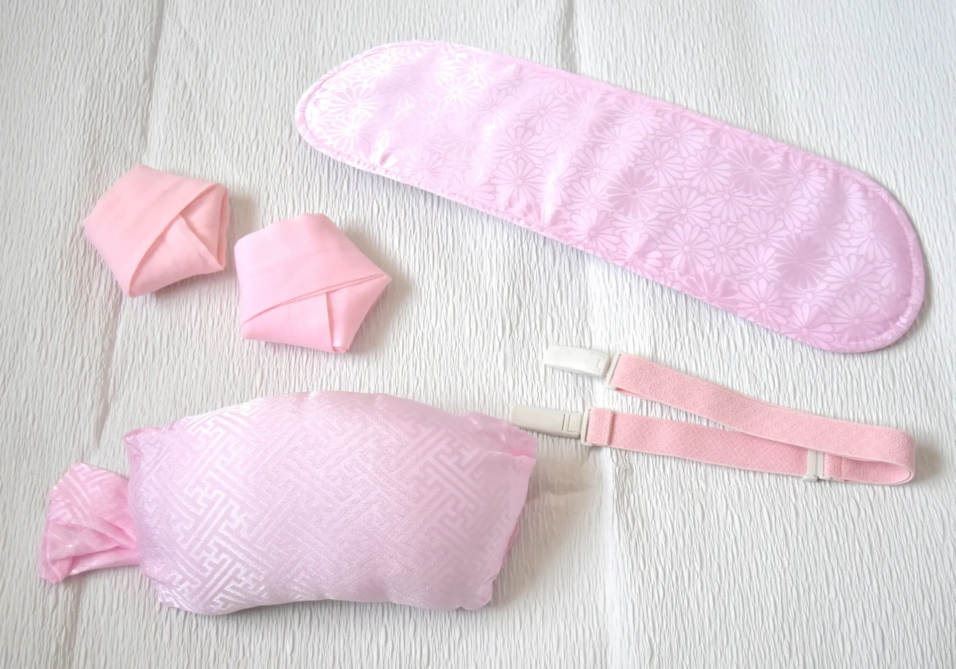 Pink fabric accessories: a long padded band with a subtle floral pattern, a rectangular pillow with a geometric pattern