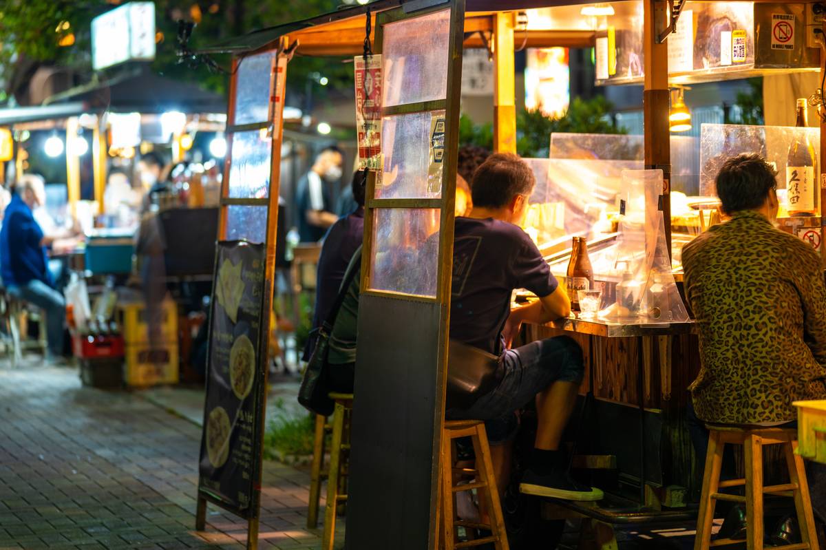 Diners at brightly lit outdoor food stalls at night.