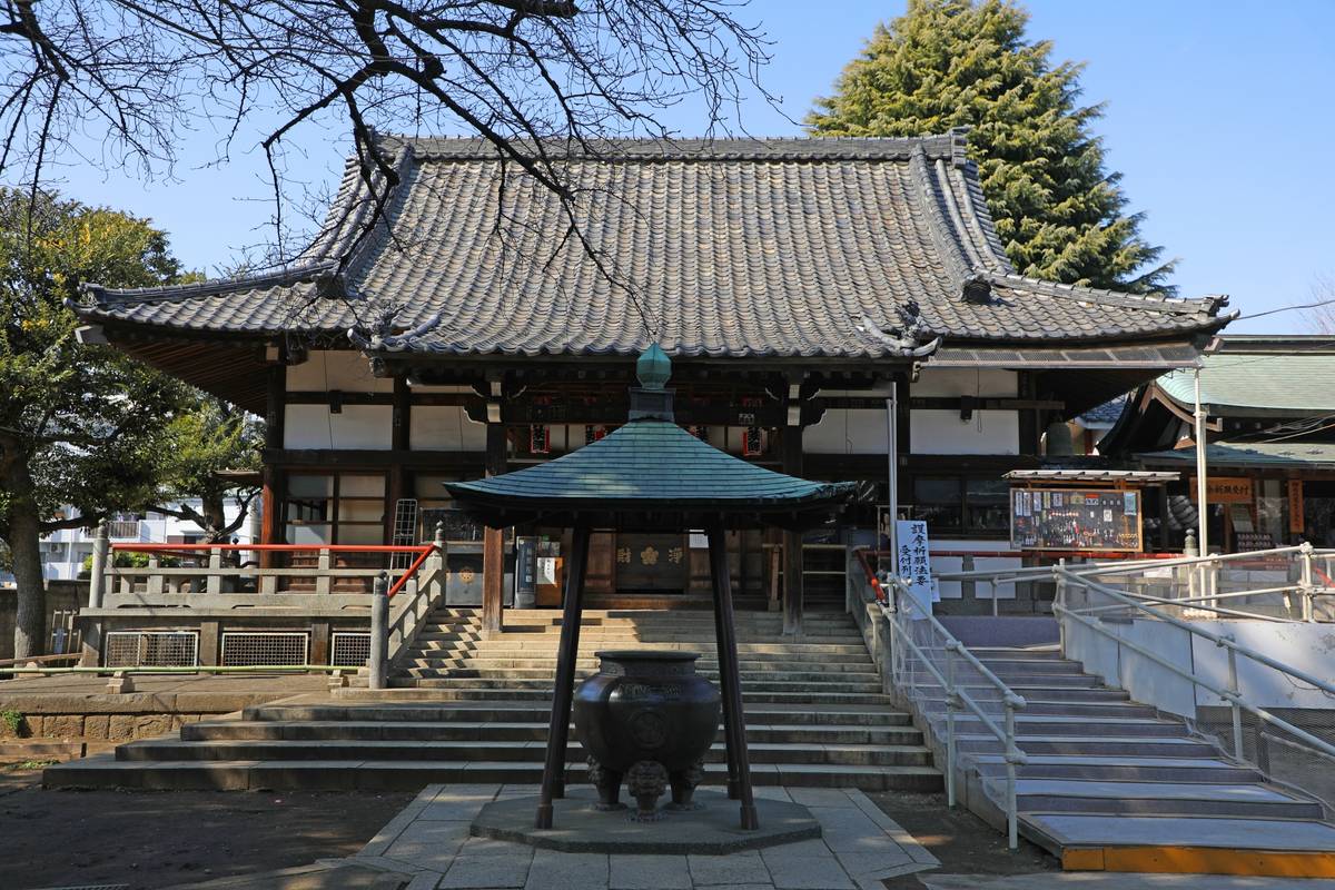 A Japanese temple with a dark tiled roof, an ornate incense burner in front, and stairs leading up to its entrance.