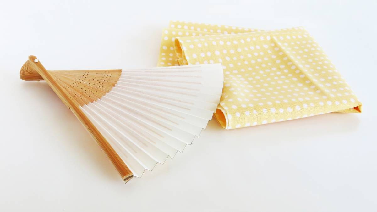 A partially open wooden and white hand fan next to a folded yellow polka-dot cloth.