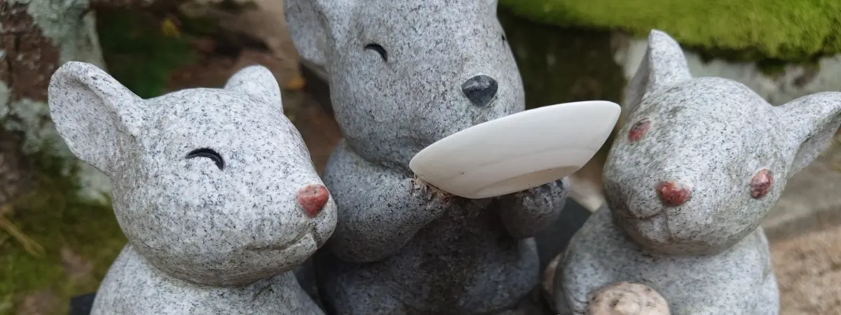 Three smiling stone mouse figures, one holding a small white dish.