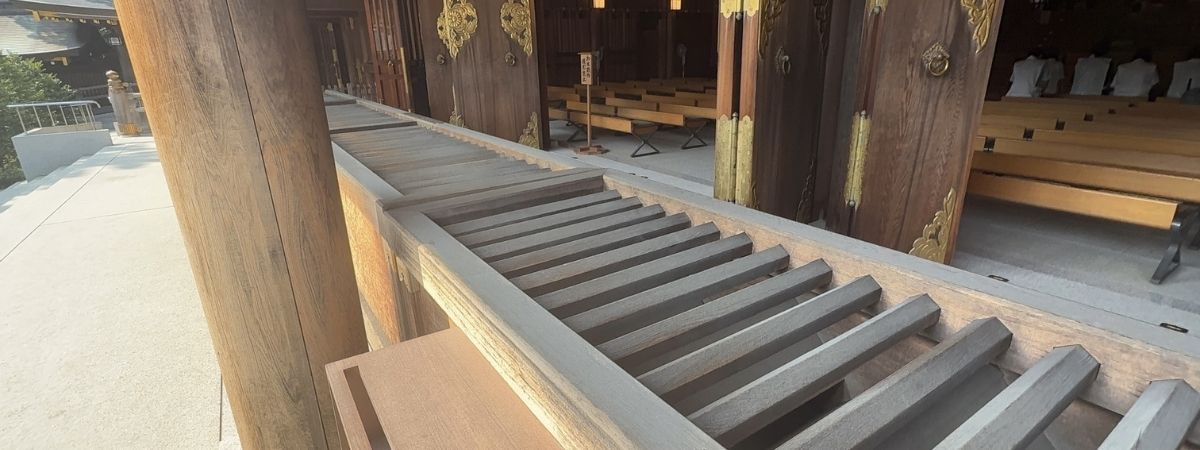 A wooden temple entrance with ornate doors and benches inside, framed by a slatted railing.