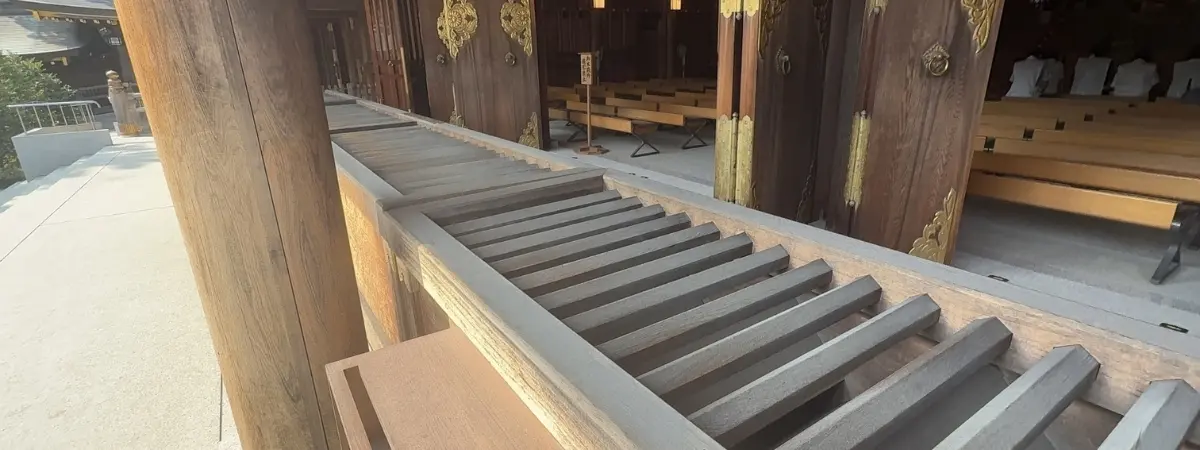 A wooden temple entrance with ornate doors and benches inside, framed by a slatted railing.