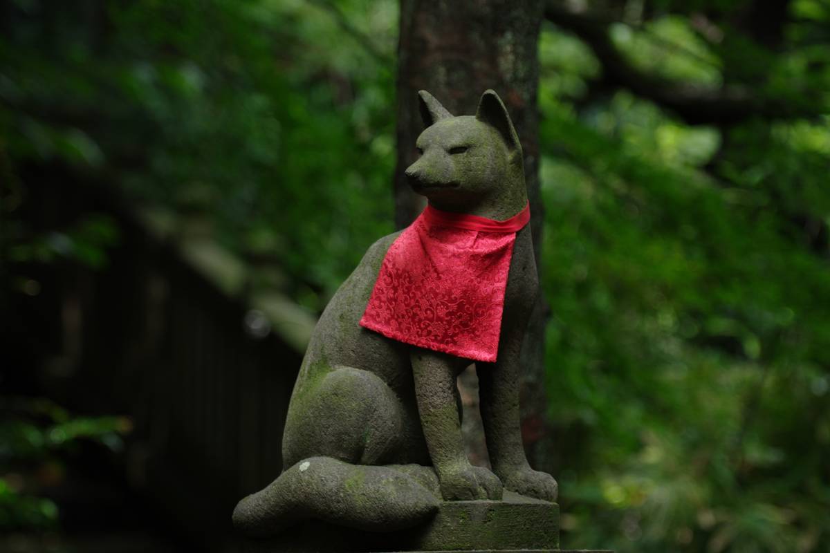 Mossy stone fox statue wearing a red bib.