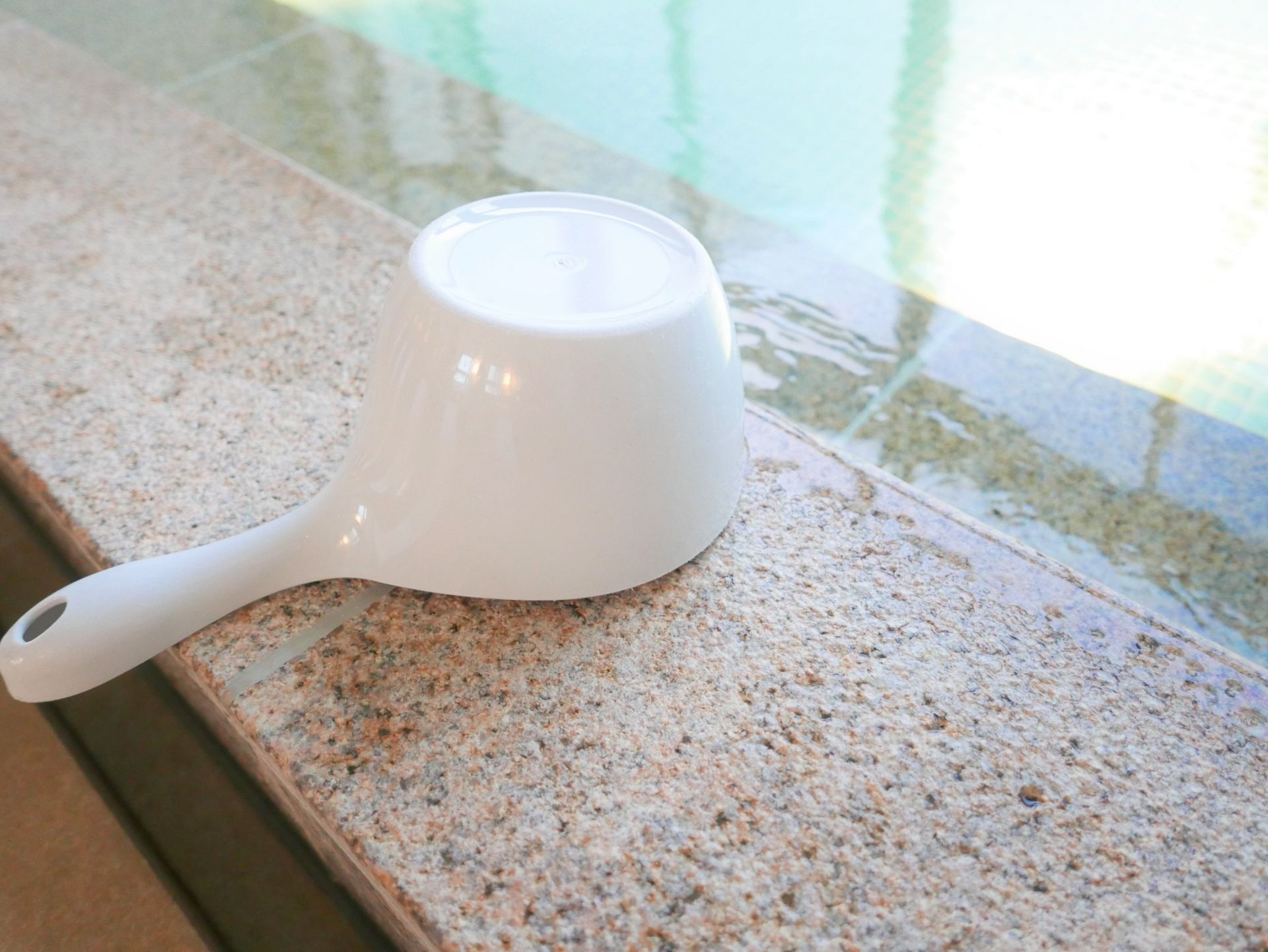 White plastic dipper on a stone ledge by a pool.