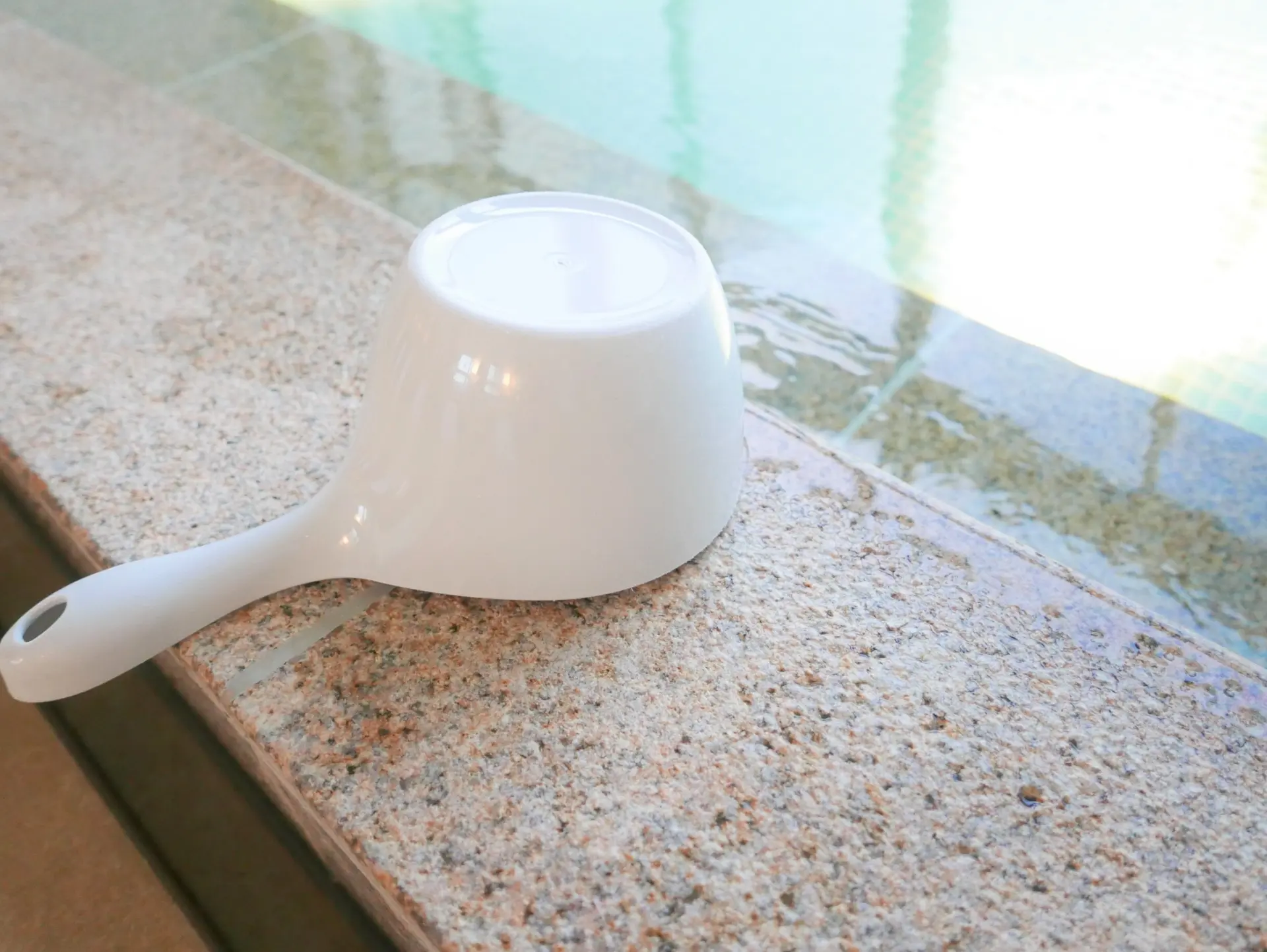 White plastic dipper on a stone ledge by a pool.