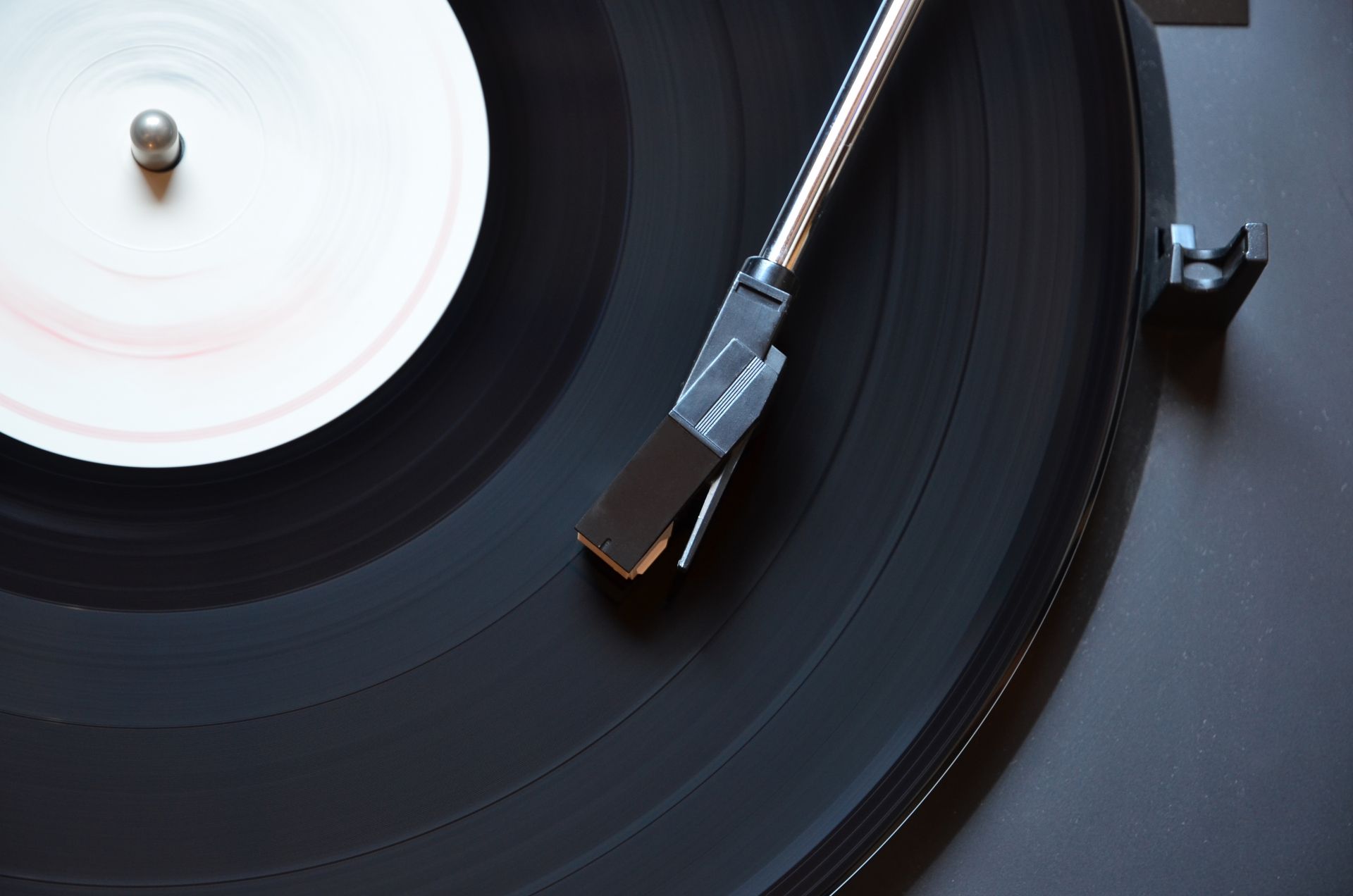 A black vinyl record with a white blurred label spinning on a turntable, with the tonearm positioned above it.