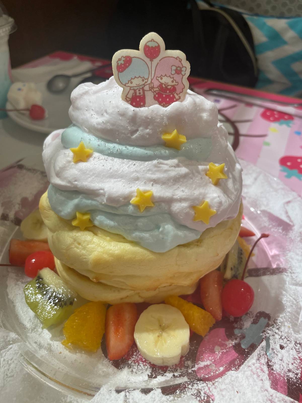 A stack of fluffy pancakes topped with pink and blue whipped cream, yellow stars, a Little Twin Stars cookie