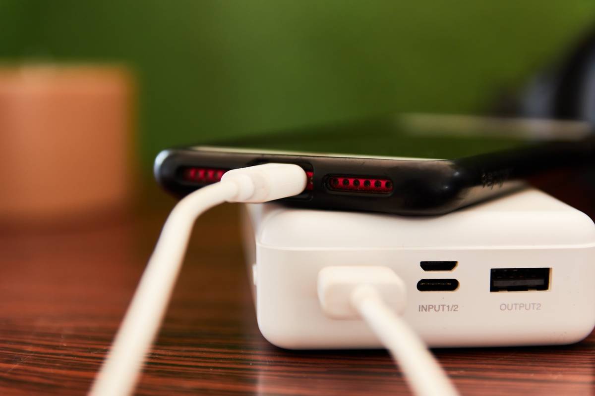 A smartphone charging on a white power bank with cables connected.