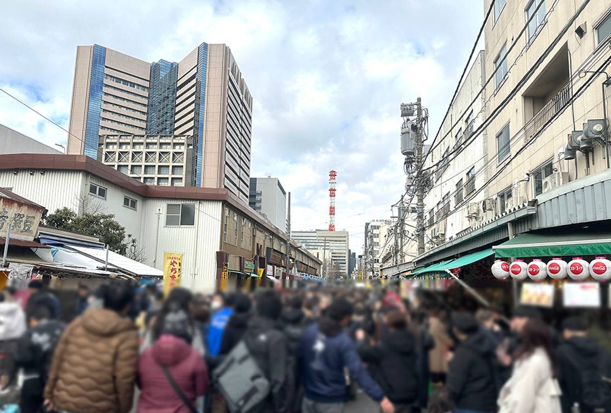 A busy shopping street with a blurred crowd, lined with shops, and a modern high-rise in the background.