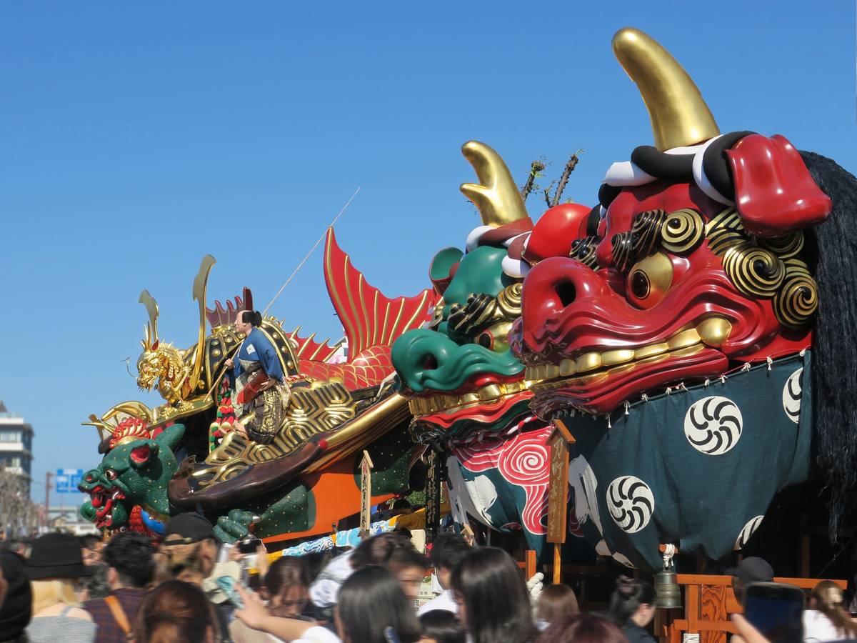 Vibrant Japanese festival floats with large red and green lion-dog heads and golden dragons.