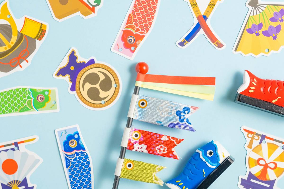A collection of colorful Japanese Children's Day decorations, including koinobori, samurai helmets, and fans, on a light blue background.