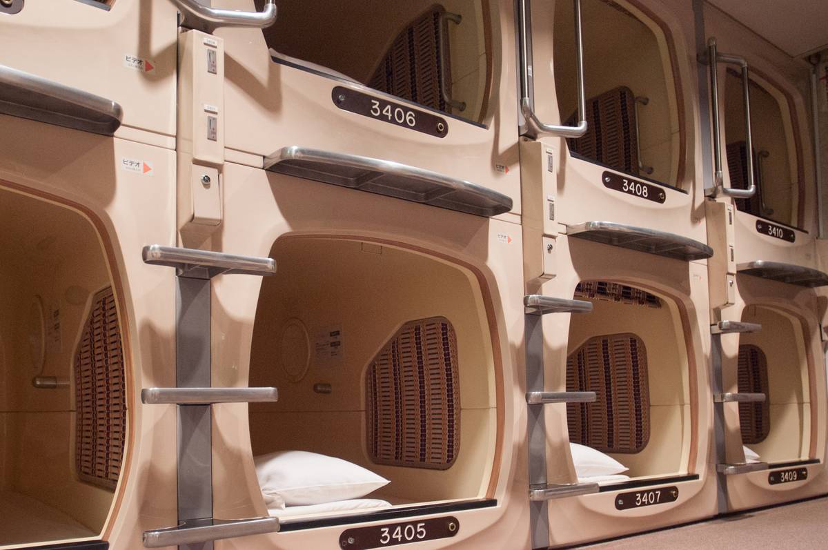 Numbered beige capsule hotel pods stacked in rows, some with pillows visible.
