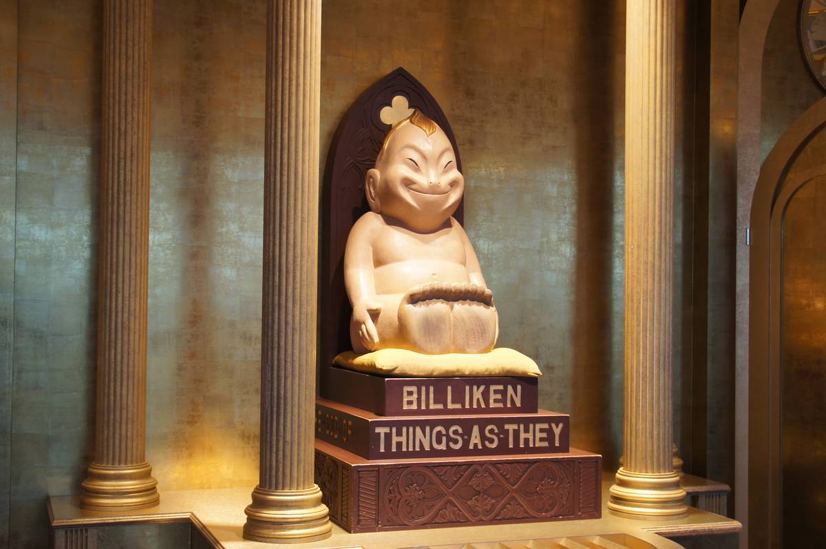 A smiling Billiken statue sits on a pedestal that reads "BILLIKEN THINGS AS THEY", flanked by golden columns.