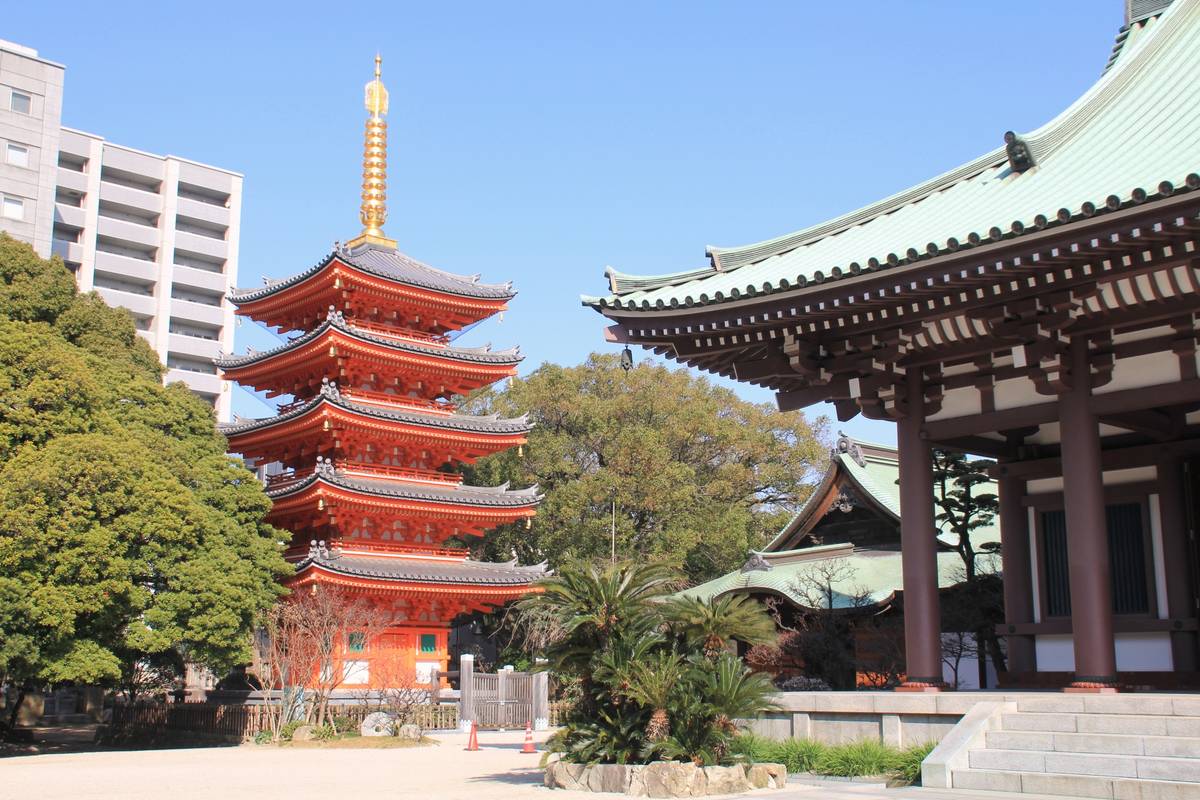 A Japanese temple complex featuring a red five-story pagoda and a large building with a green roof.
