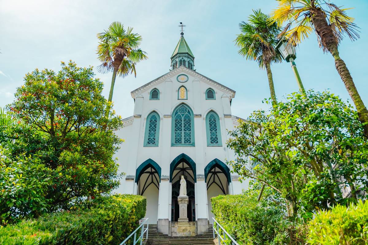 A white church with a green spire, arched blue windows, and a statue at its entrance