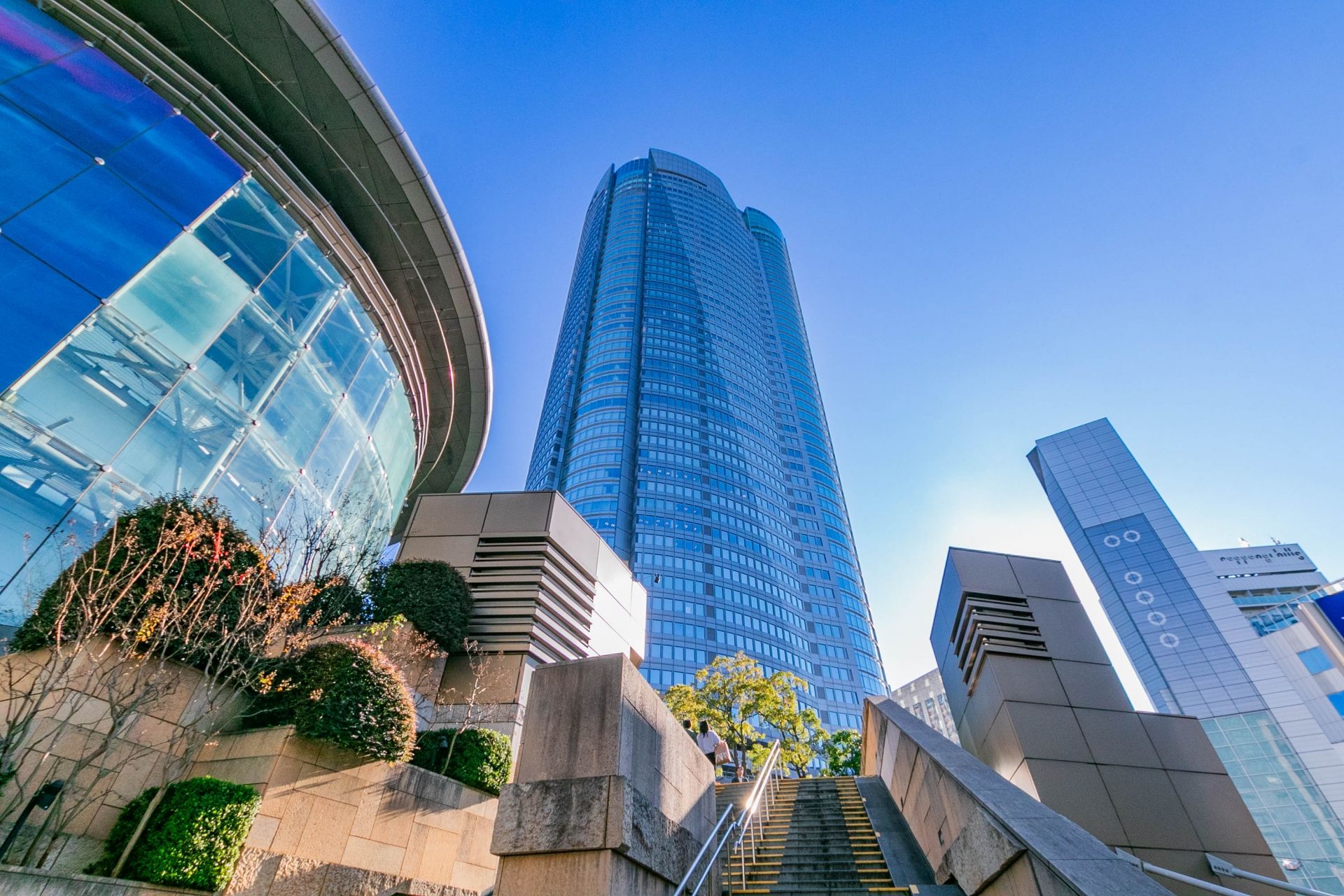 Low-angle view of Roppongi Hills Mori Tower and a curving glass building under a clear blue sky