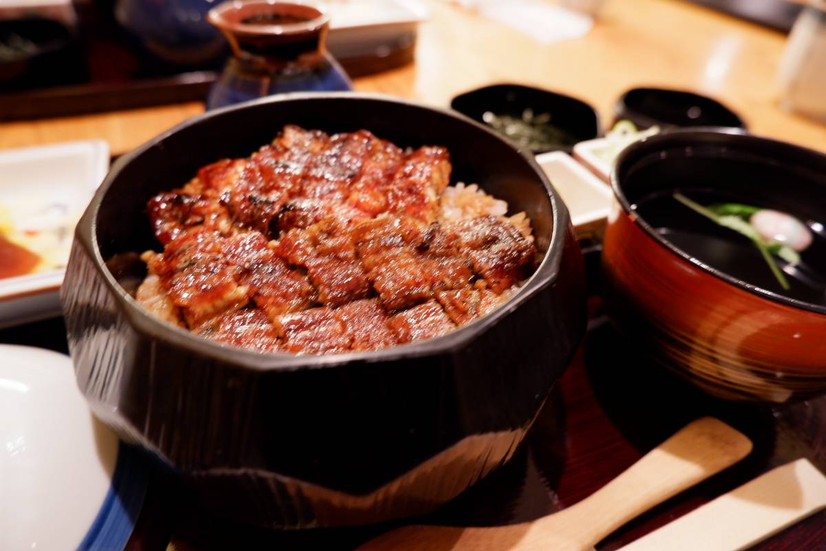 Grilled unagi (eel) over rice in a dark bowl, with a side of soup.