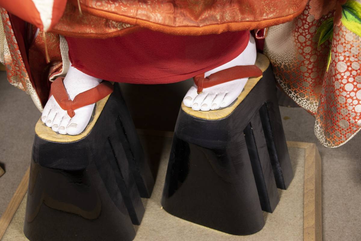 Doll's white feet in red thong sandals on tall black platform shoes, under a kimono.