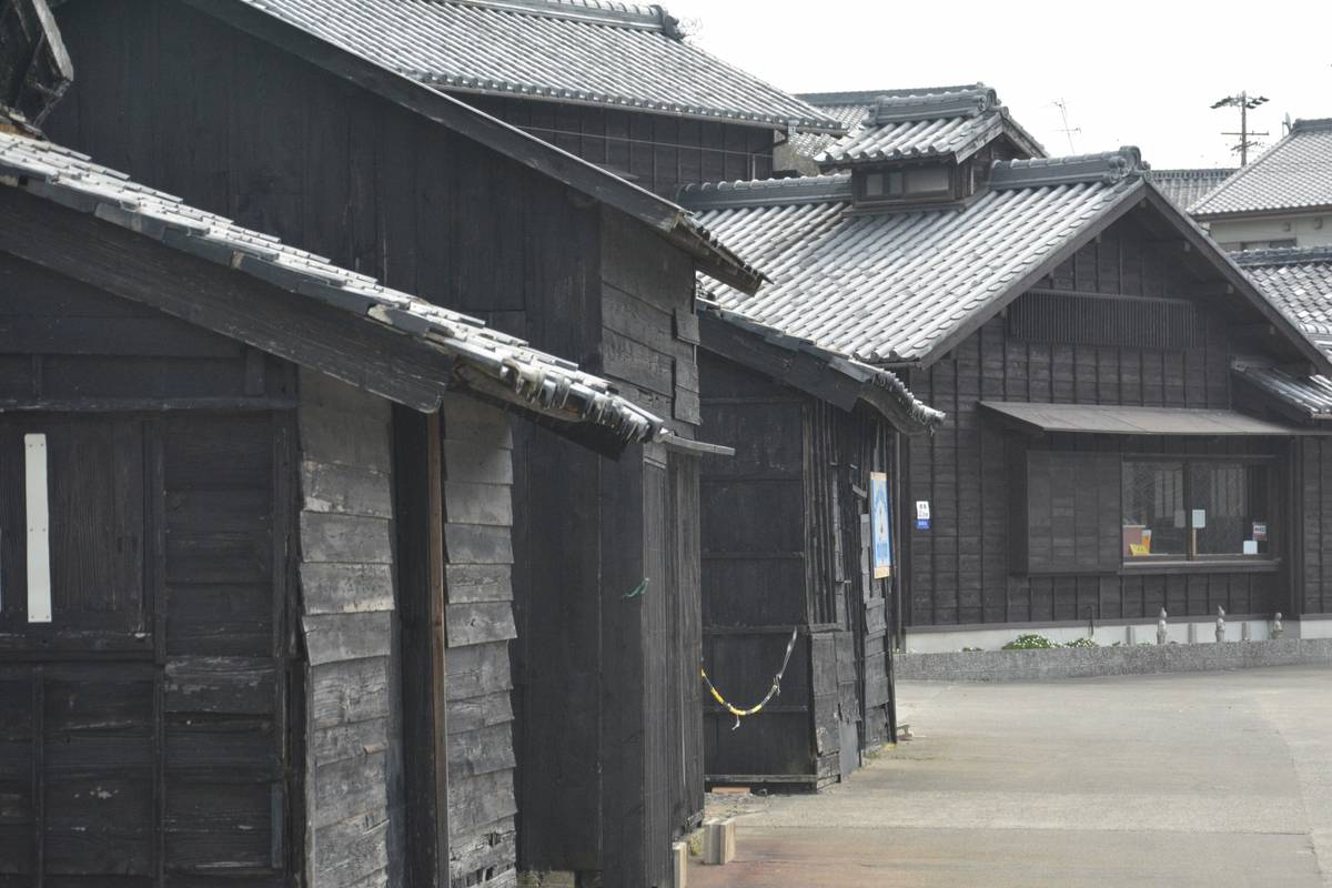 Row of traditional Japanese buildings with dark wooden facades and gray tiled roofs along a path.