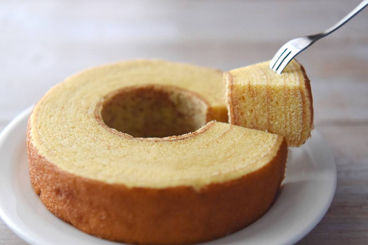 A layered Baumkuchen cake on a plate with a fork lifting a slice.