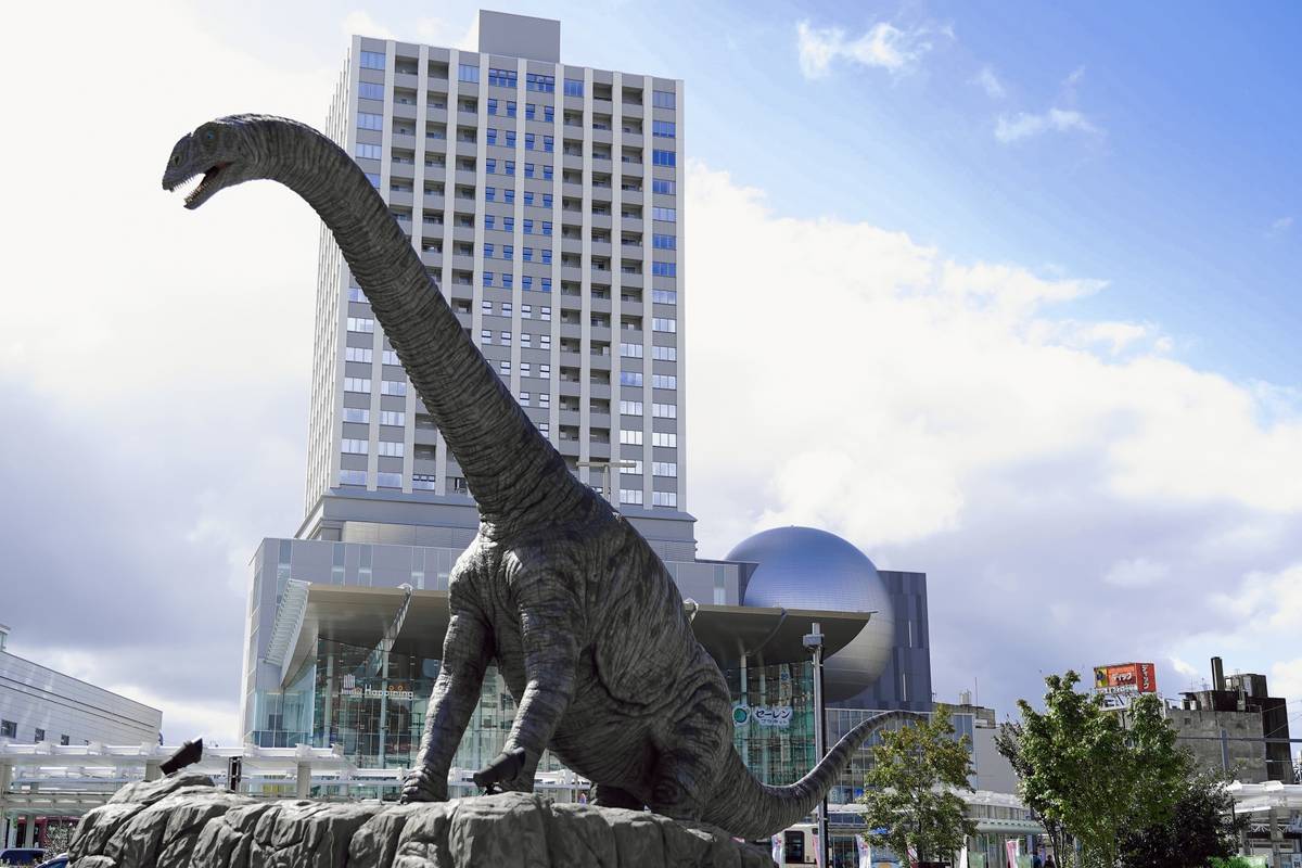 Brachiosaurus statue in front of a modern building and spherical dome.