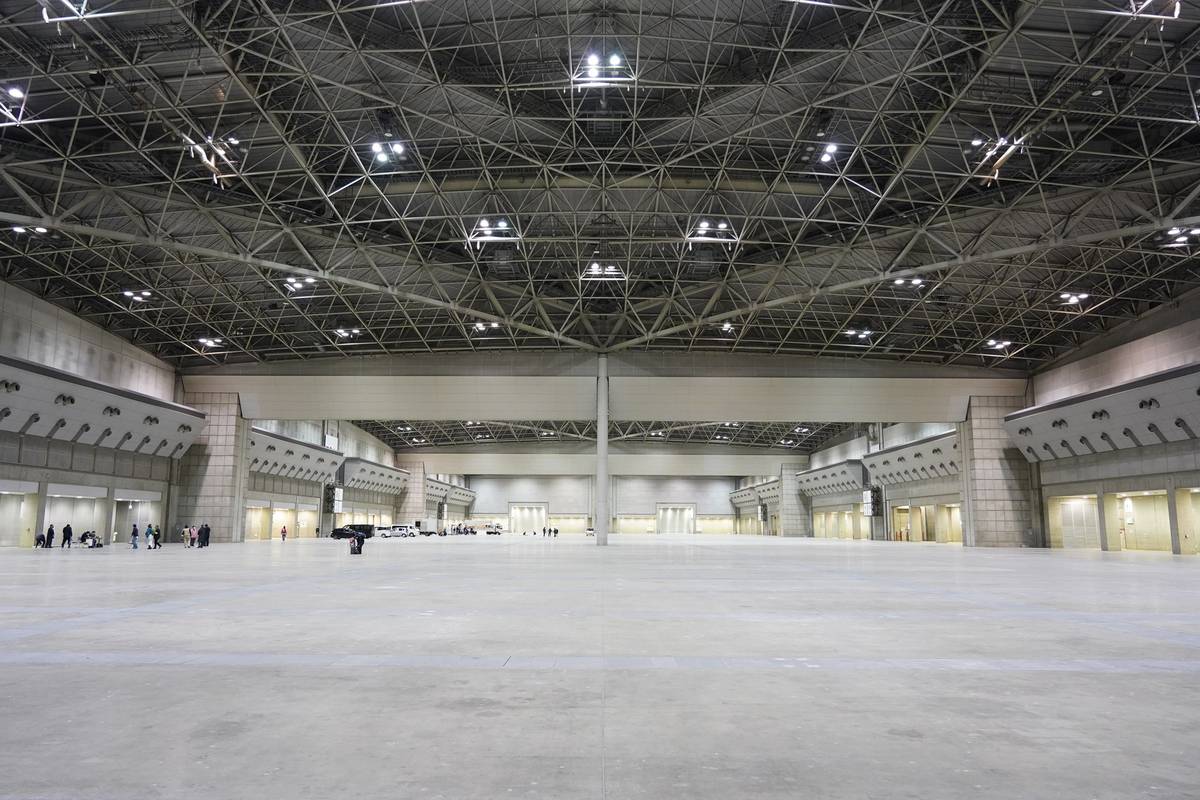 Vast, empty exhibition hall with a high, exposed metal truss ceiling.