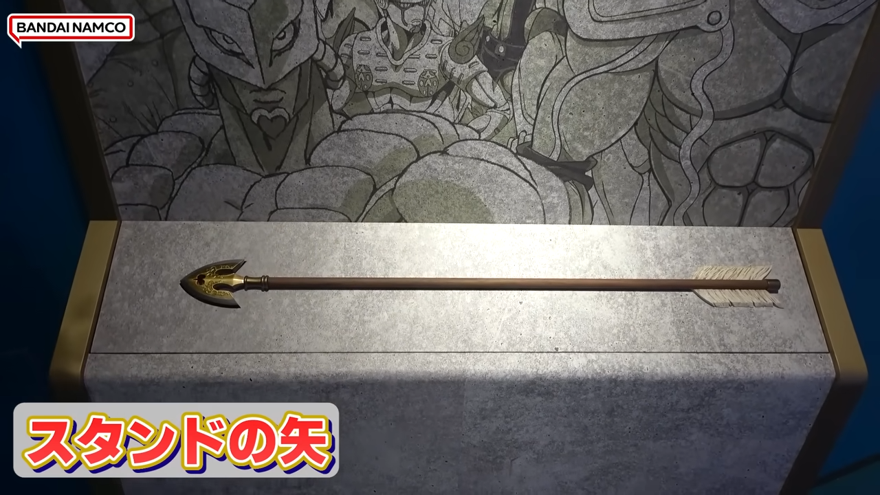 A gold-tipped Stand Arrow prop on a display stand, backed by stylized anime character art.