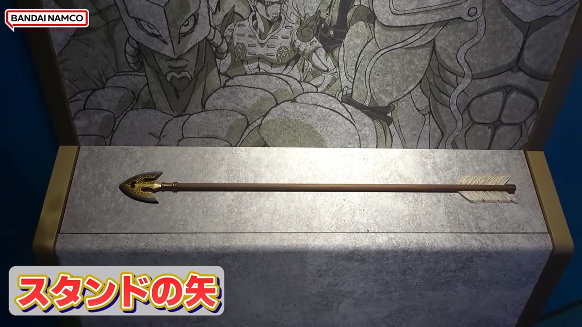 A gold-tipped Stand Arrow prop on a display stand, backed by stylized anime character art.
