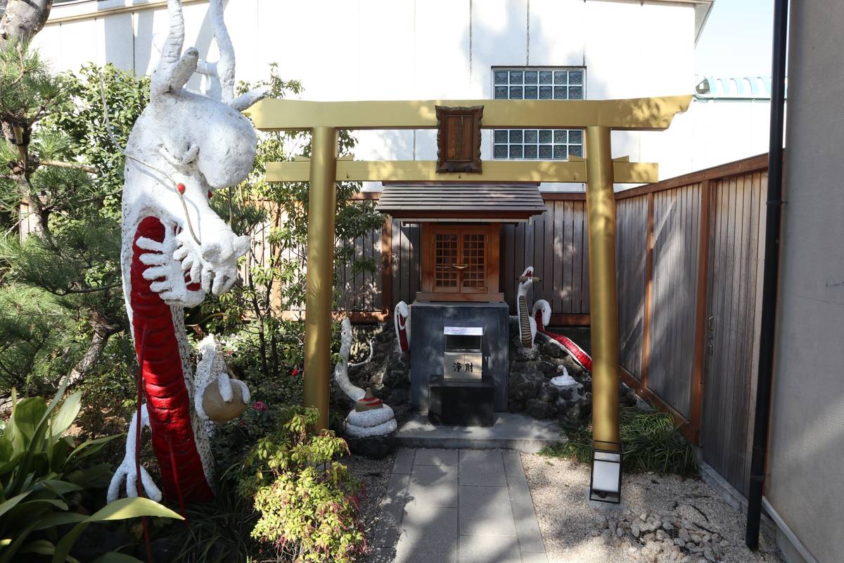 A white and red dragon statue next to a golden torii gate leading to a small wooden shrine.