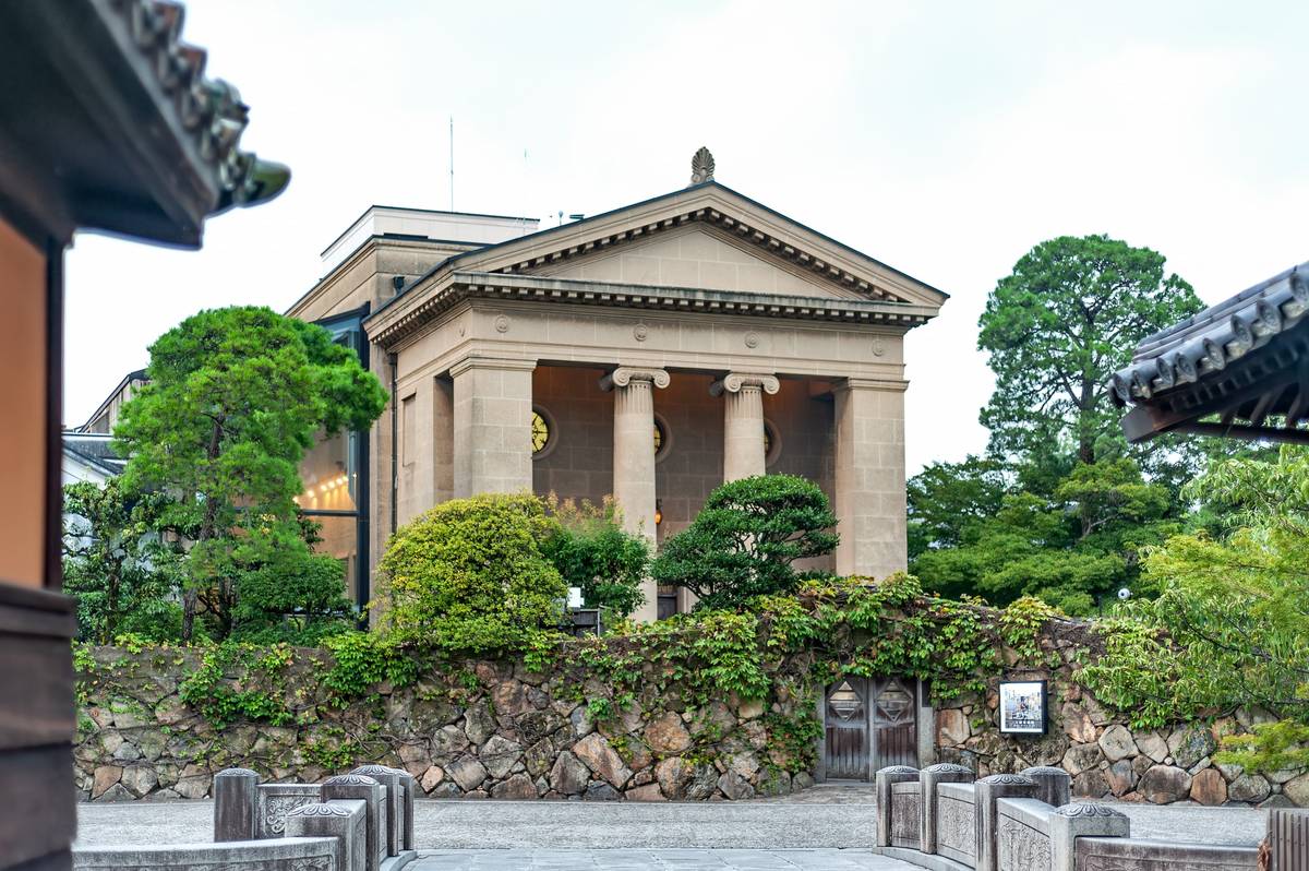 A classical building with columns and a pediment, behind an ivy-covered stone wall