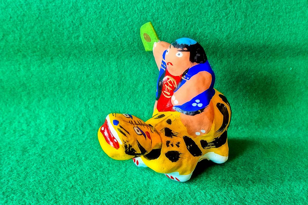 Colorful figurine of a boy riding a striped tiger on a green background.