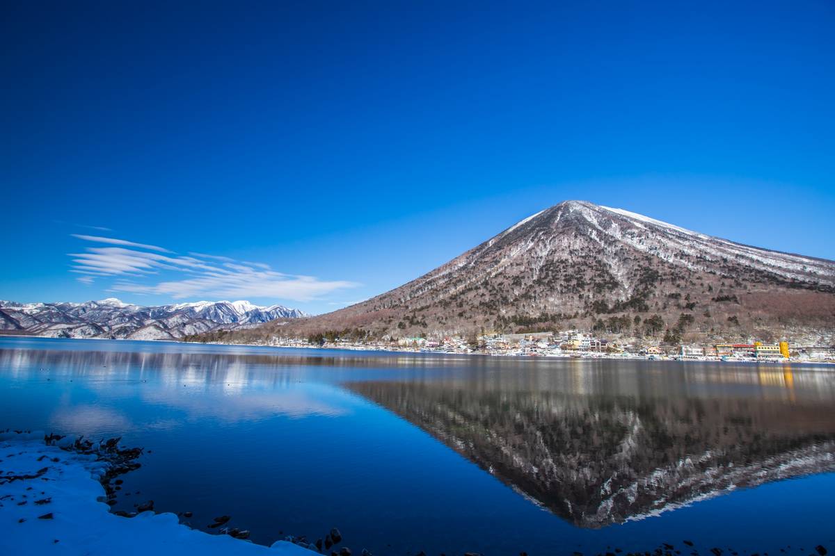 Snow-capped mountain reflecting in a calm lake under a clear blue sky.